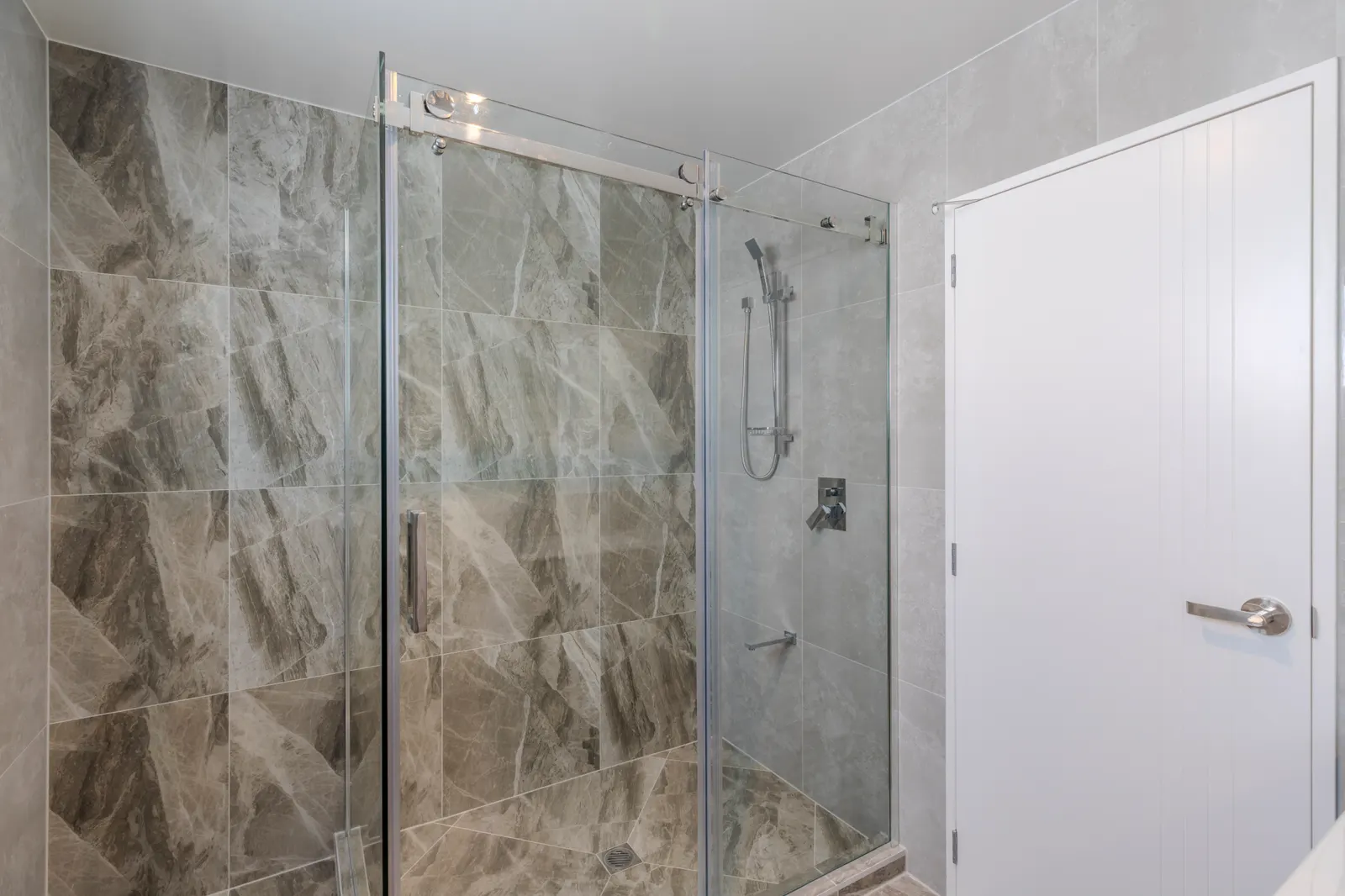 Sliding glass shower enclosure with chrome hardware against grey marble-look tile.