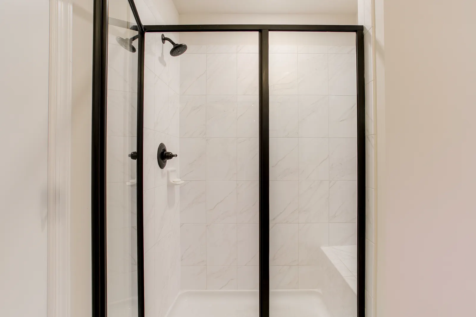 Black-framed sliding glass shower door over a white marble-tiled alcove.