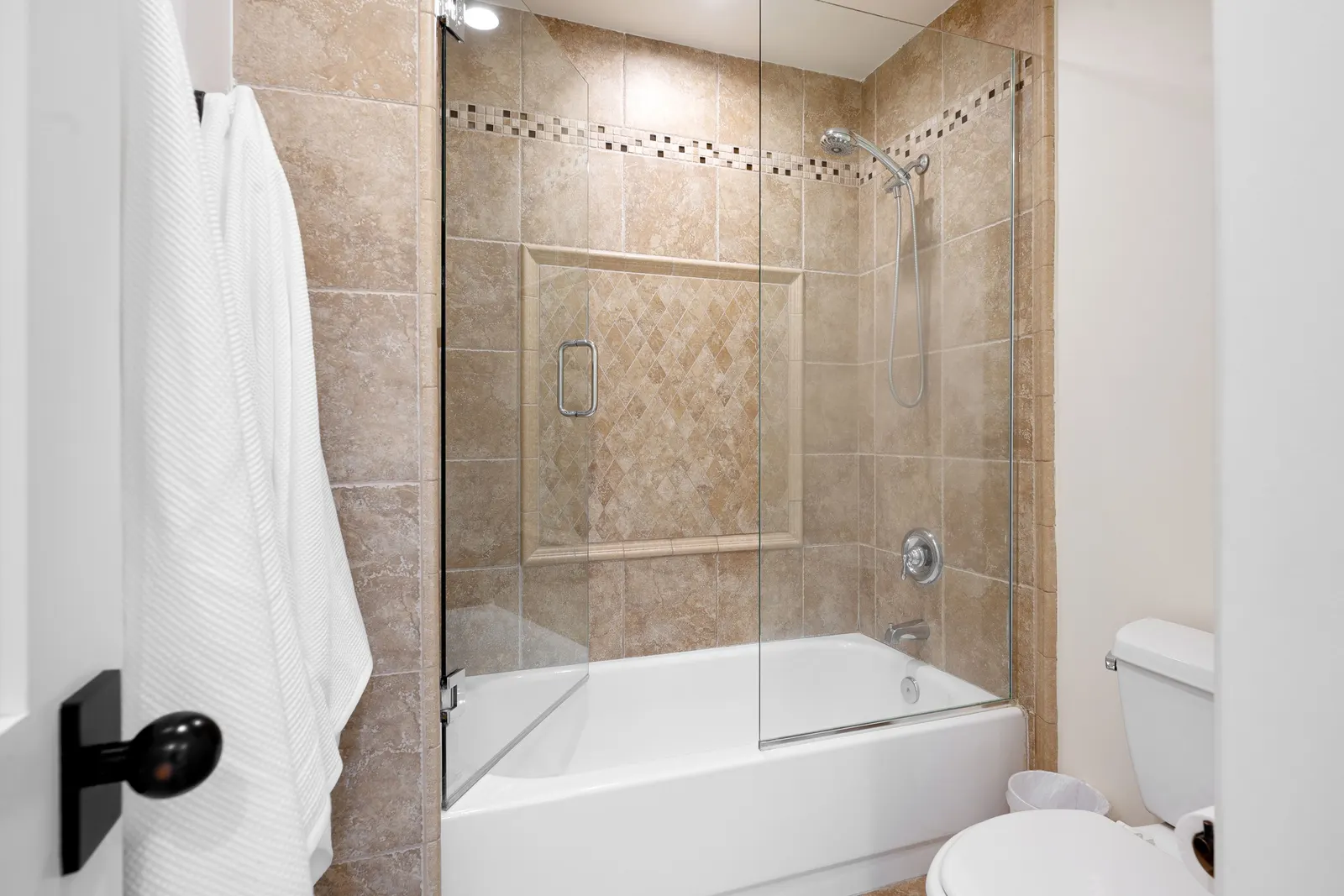 Bathtub with a frameless hinged glass bath screen and travertine tile.