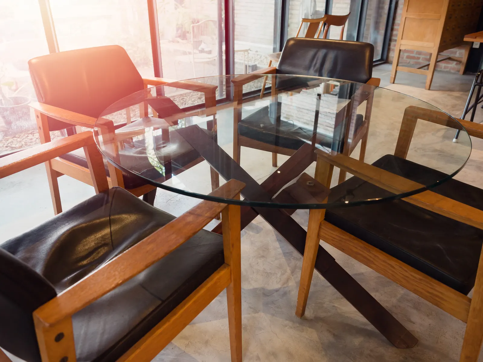 Round clear glass table top on a wooden cross-base surrounded by leather armchairs.