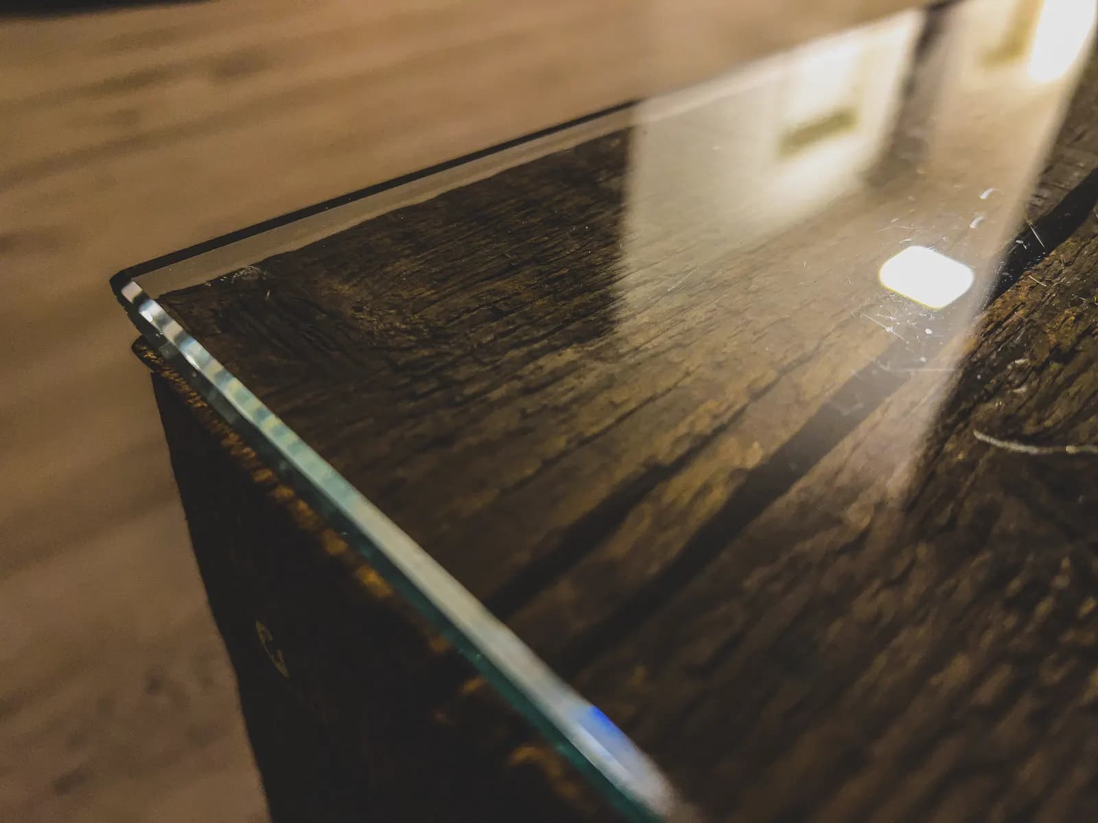Close-up of the polished edge and corner of a clear glass table top on rustic wood.