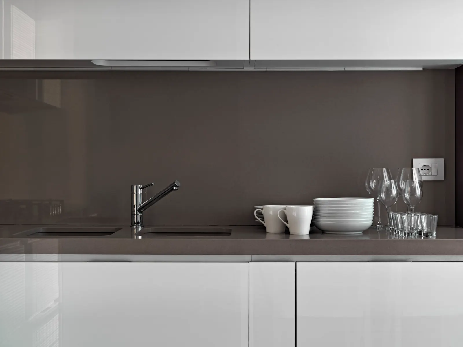 Grey glass backsplash panel behind a kitchen sink with white cabinets.